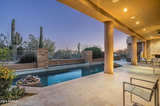 pool at dusk with ceiling fan and a patio area