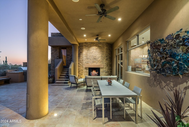 patio terrace at dusk with an outdoor stone fireplace and ceiling fan