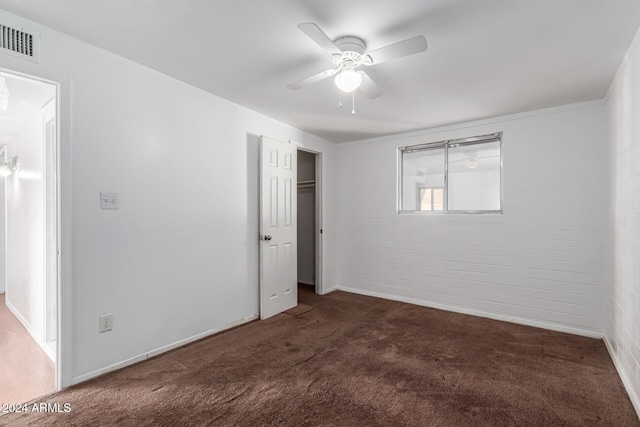 unfurnished bedroom with ceiling fan, dark carpet, brick wall, and a closet