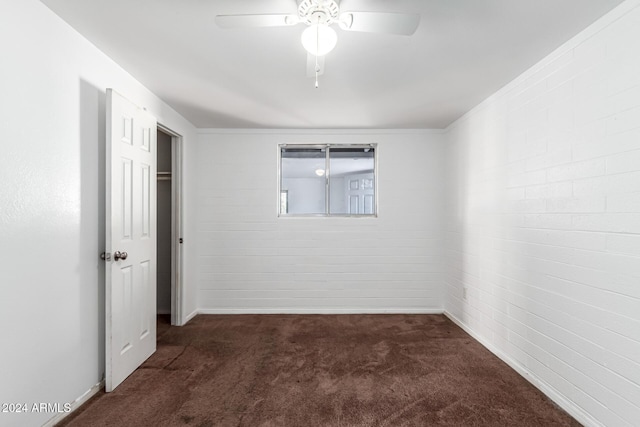 unfurnished room featuring ceiling fan, ornamental molding, brick wall, and dark colored carpet