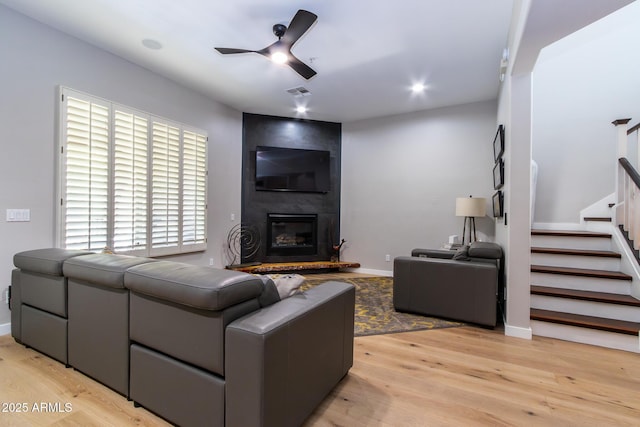 living room featuring ceiling fan, a fireplace, and light wood-type flooring