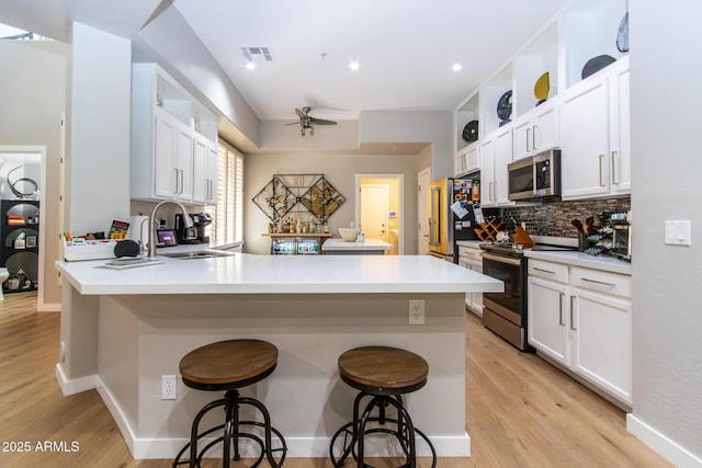 kitchen with kitchen peninsula, appliances with stainless steel finishes, a breakfast bar, ceiling fan, and white cabinets