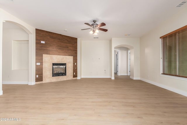 unfurnished living room with a tile fireplace, wooden walls, ceiling fan, and light hardwood / wood-style floors