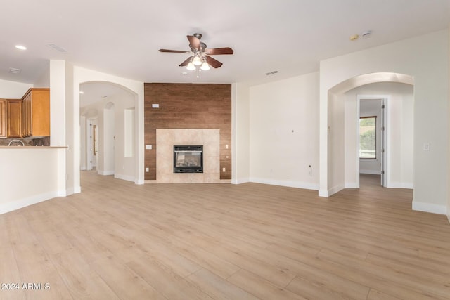 unfurnished living room with a tile fireplace, ceiling fan, and light hardwood / wood-style floors