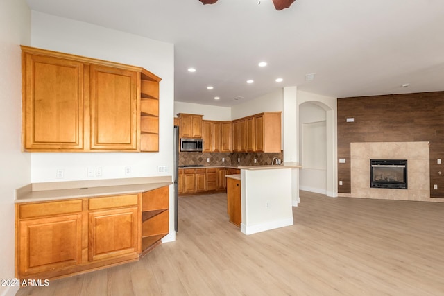 kitchen featuring a tile fireplace, ceiling fan, decorative backsplash, light wood-type flooring, and a breakfast bar area