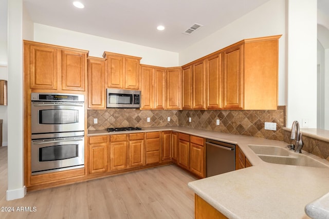 kitchen with decorative backsplash, stainless steel appliances, light hardwood / wood-style floors, and sink