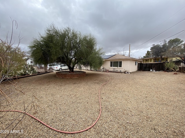 view of front of home featuring roof mounted solar panels, stucco siding, and fence