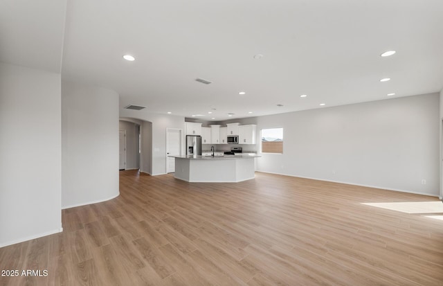 unfurnished living room with arched walkways, recessed lighting, visible vents, and light wood-style floors