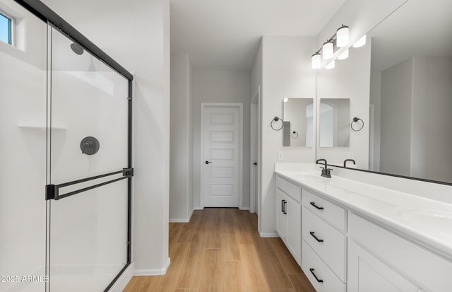 full bathroom with a sink, wood finished floors, baseboards, double vanity, and a stall shower