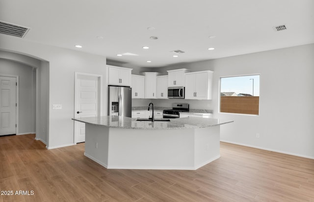 kitchen featuring appliances with stainless steel finishes, white cabinetry, a center island with sink, and a sink