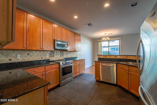 kitchen featuring sink, dark tile patterned floors, stainless steel appliances, tasteful backsplash, and a chandelier