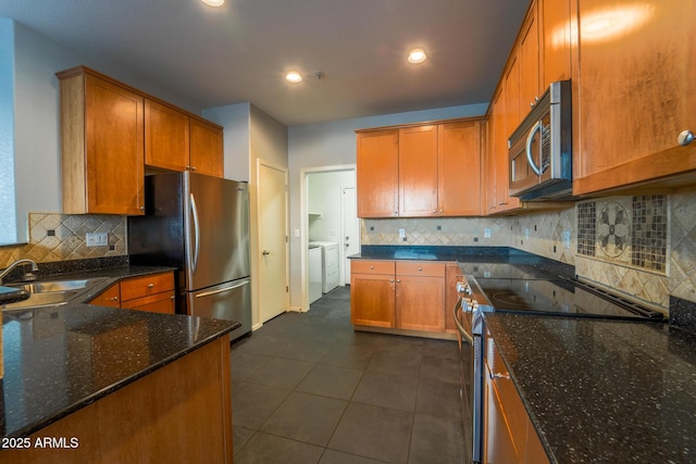 kitchen with sink, dark stone countertops, stainless steel appliances, independent washer and dryer, and dark tile patterned flooring