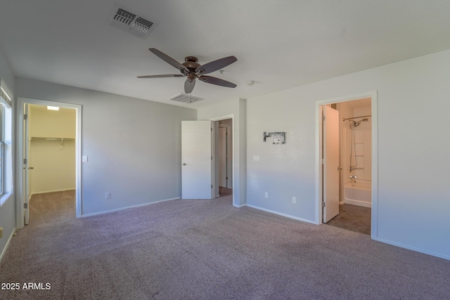 unfurnished bedroom with ensuite bathroom, a walk in closet, carpet flooring, and ceiling fan