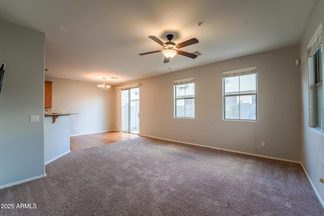 unfurnished living room with ceiling fan with notable chandelier and light colored carpet