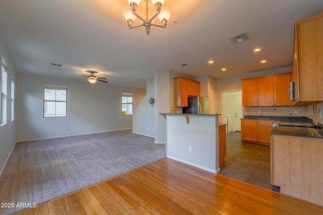 kitchen with a breakfast bar, tasteful backsplash, kitchen peninsula, stainless steel appliances, and ceiling fan with notable chandelier