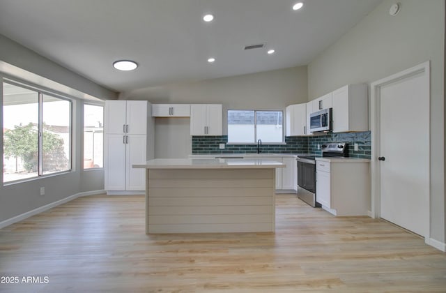 kitchen featuring decorative backsplash, lofted ceiling, a kitchen island, white cabinetry, and stainless steel appliances