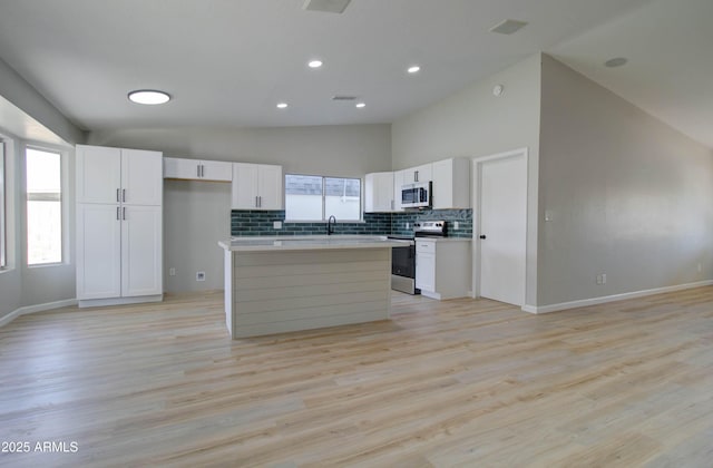 kitchen with white cabinets, appliances with stainless steel finishes, a sink, a center island, and decorative backsplash