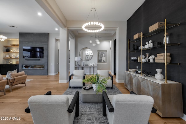 living room with a fireplace, a notable chandelier, light wood-style floors, and baseboards