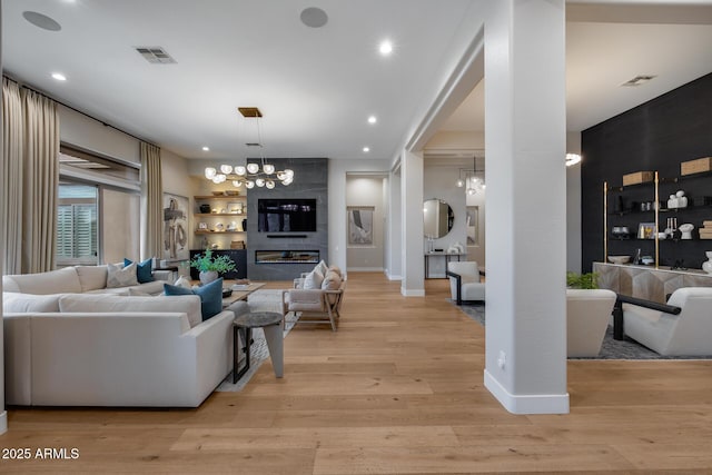 living area with visible vents, baseboards, a chandelier, and light wood finished floors