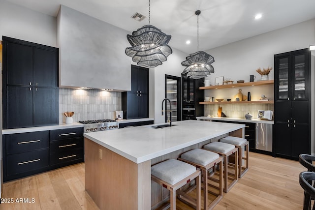 kitchen featuring a center island with sink, a kitchen bar, light countertops, dark cabinetry, and a sink