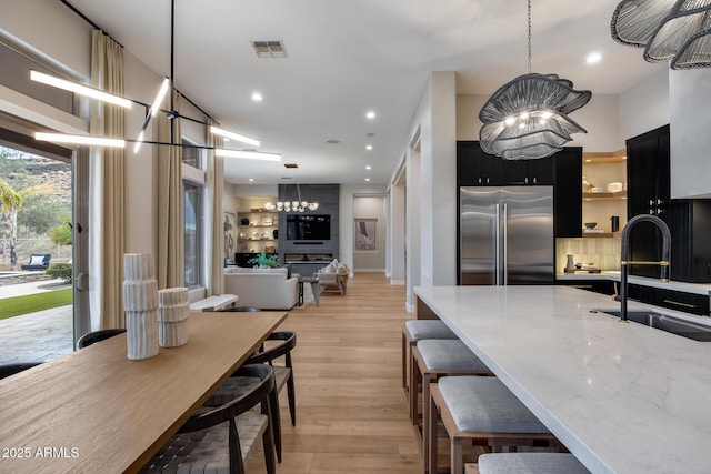 kitchen with visible vents, a chandelier, dark cabinets, stainless steel built in fridge, and a sink