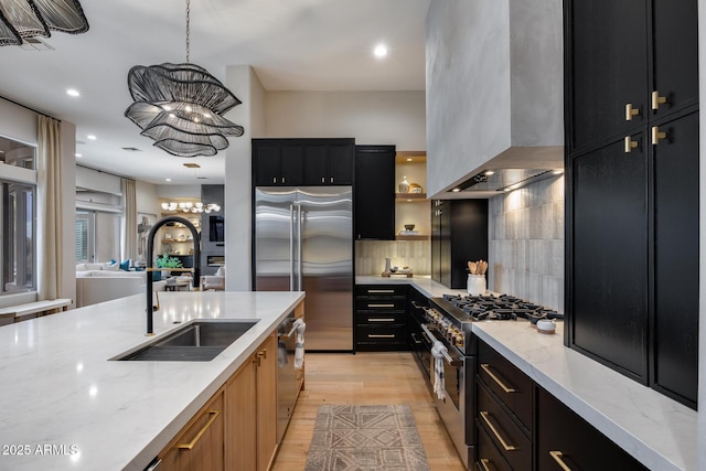 kitchen featuring a sink, light wood-style floors, wall chimney range hood, high quality appliances, and dark cabinets