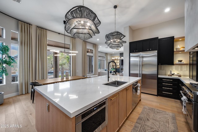 kitchen featuring dark cabinetry, a center island with sink, a sink, light countertops, and premium appliances