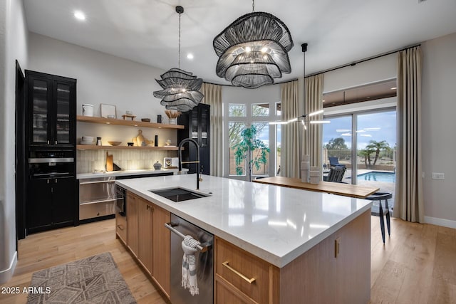 kitchen featuring dishwasher, light wood-style flooring, a center island with sink, and a sink