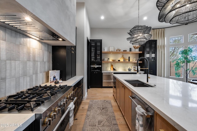 kitchen with light wood-type flooring, a sink, tasteful backsplash, stainless steel appliances, and wall chimney range hood