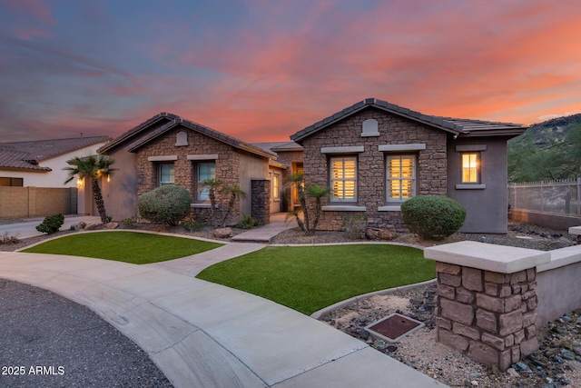 view of front of home featuring stone siding, a tile roof, a front lawn, and fence