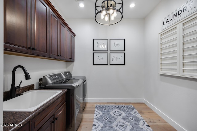 clothes washing area featuring baseboards, washing machine and dryer, light wood-style floors, cabinet space, and a sink