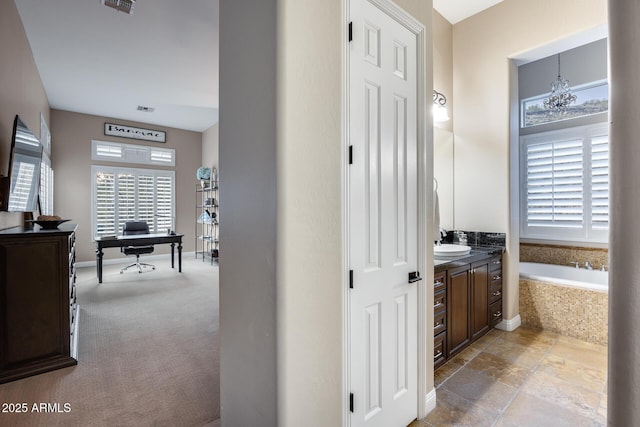 bathroom with a wealth of natural light, a notable chandelier, a garden tub, and vanity