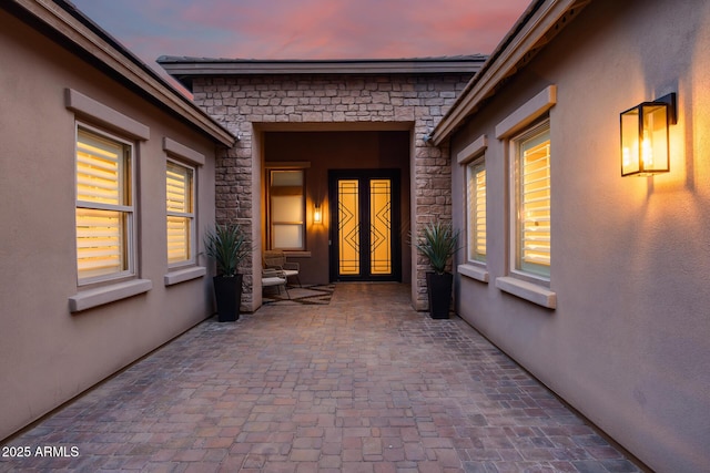 property entrance with stucco siding, stone siding, and a patio