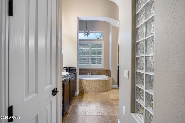 bathroom featuring a textured wall, stone tile flooring, vanity, and a bath