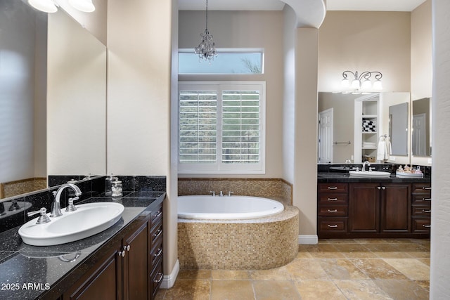 bathroom featuring a notable chandelier, two vanities, a bath, and a sink