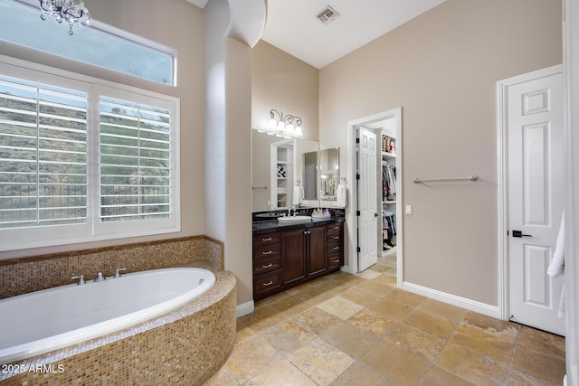 bathroom featuring a spacious closet, visible vents, a garden tub, stone tile floors, and vanity