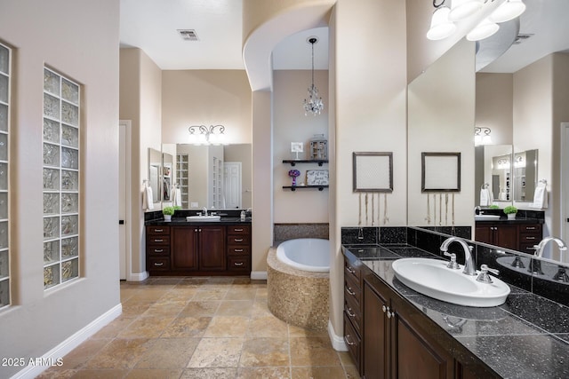 bathroom featuring a garden tub, two vanities, visible vents, and a sink