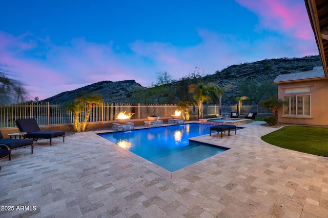 pool at dusk featuring a mountain view, a fire pit, a fenced in pool, an in ground hot tub, and a patio area