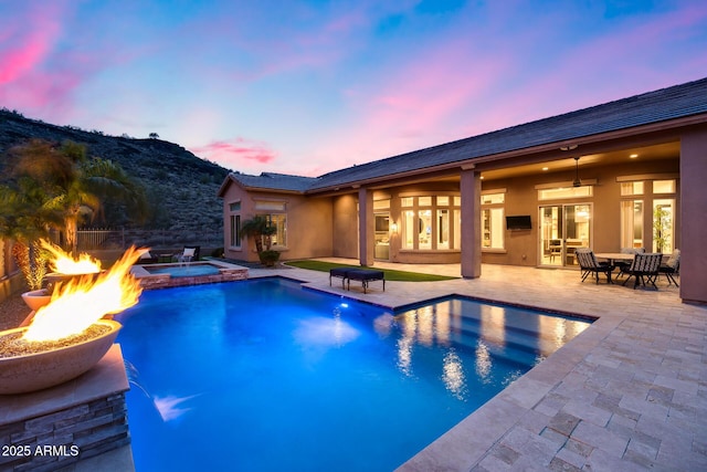 view of pool with a pool with connected hot tub, an outdoor fire pit, a mountain view, ceiling fan, and a patio area