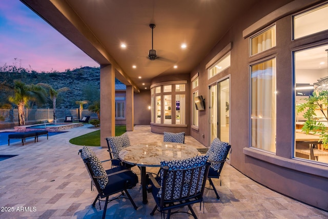 patio terrace at dusk with outdoor dining space, a fenced in pool, fence, an in ground hot tub, and ceiling fan