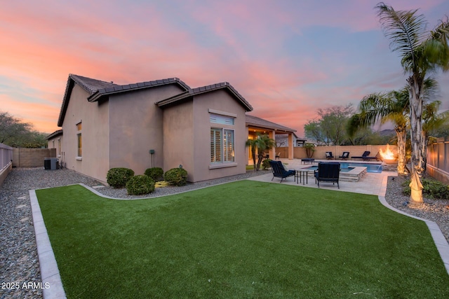 back of house at dusk with central AC, stucco siding, a yard, a fenced backyard, and a patio area