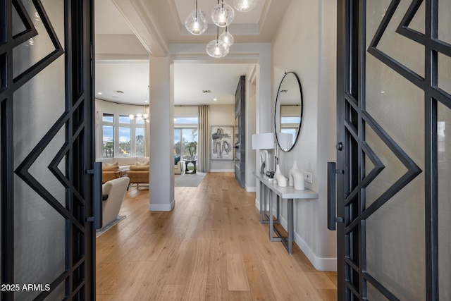 foyer entrance with baseboards, light wood finished floors, and a chandelier