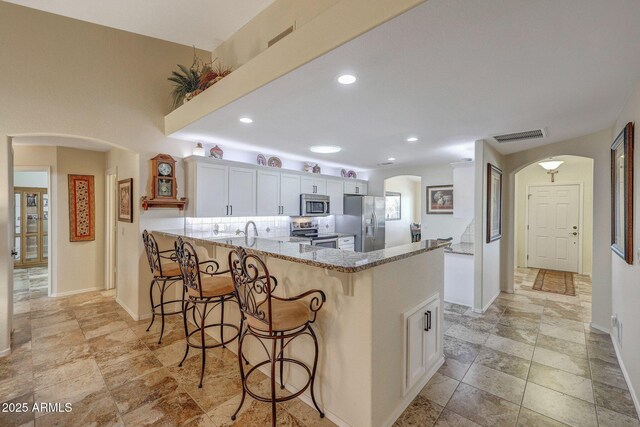 11047 W Irma Ln, Peoria, AZ 85373 - kitchen with light stone counters, a kitchen breakfast bar, a peninsula, stainless steel appliances, and arched walkways