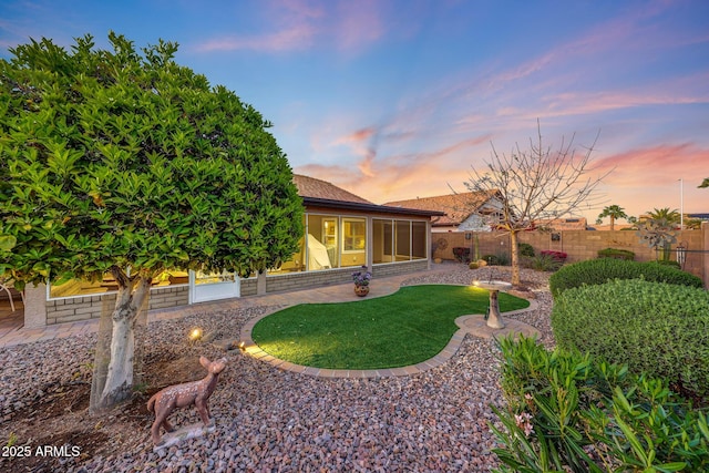 11047 W Irma Ln, Peoria, AZ 85373 - yard at dusk featuring a fenced backyard, a sunroom, and a patio