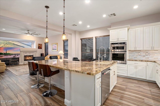 kitchen with decorative light fixtures, a center island with sink, stainless steel appliances, visible vents, and open floor plan