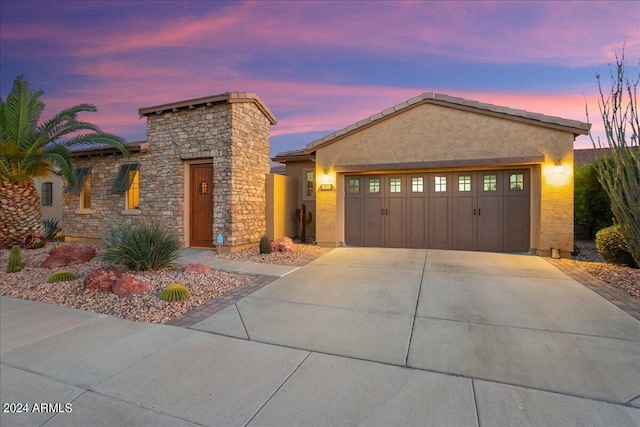 view of front of home with stone siding, driveway, an attached garage, and stucco siding