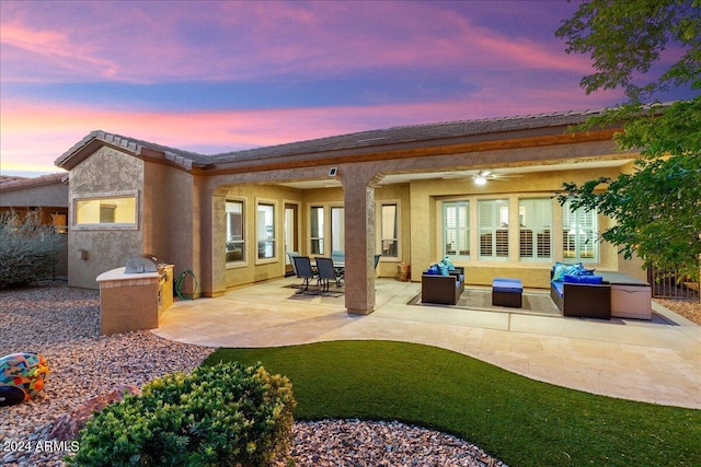 back of property featuring an outdoor kitchen, a ceiling fan, an outdoor living space, stucco siding, and a patio area