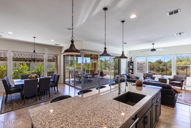 kitchen with a kitchen island with sink, sink, hanging light fixtures, light stone countertops, and ceiling fan