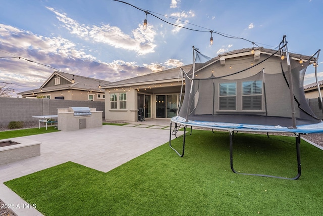 back of house with exterior kitchen, a patio area, a yard, and a trampoline