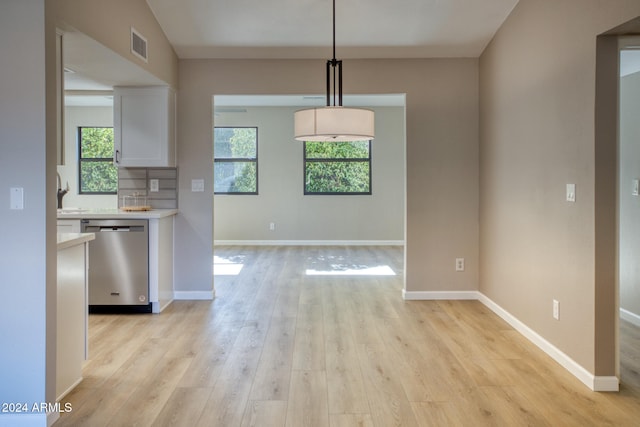 kitchen with light hardwood / wood-style floors, white cabinetry, backsplash, stainless steel dishwasher, and pendant lighting